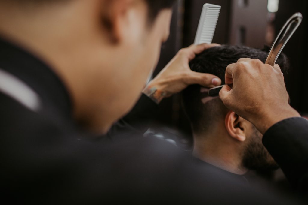 empleado barberia afeitando a un cliente brindando el servicio de corte de pelo en salón de belleza